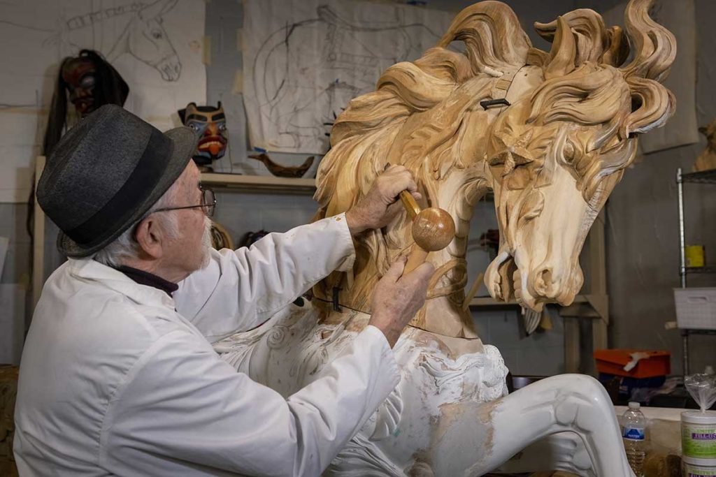 man carving wooden carousel hippocampus